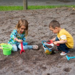 Ein Mädchen und ein Junge sitzen im Sand uns spielen